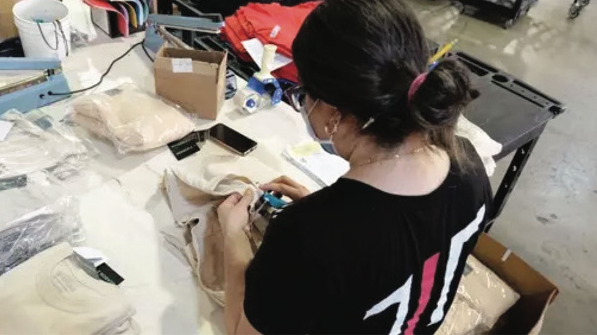 A Thrive worker applies a tag to a t-shirt, without automation.